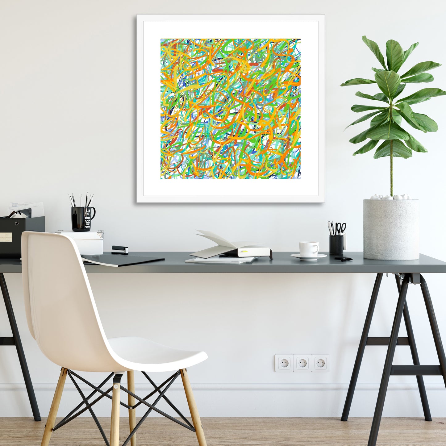 In a white room above a modern grey and black desk with white chair and desk accessories hangs 'Fishing Boats On The Beach' with bright yellows, reds and greens tangled together with sky-blue, sea-blues and greens - with white mount in white frame.
