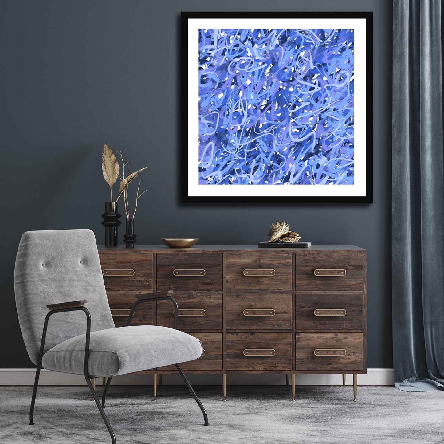 The black-framed 'A Touch Of Frost' stands out with the darker tones of this room. The wall is grey-blue with matching velvet curtain to one side and below the art, a multi-drawer natural wood sideboard with gold pull handles. In the foreground, a modern pale blue velvet-covered chair, again picking up on the frosty blues of the artwork.